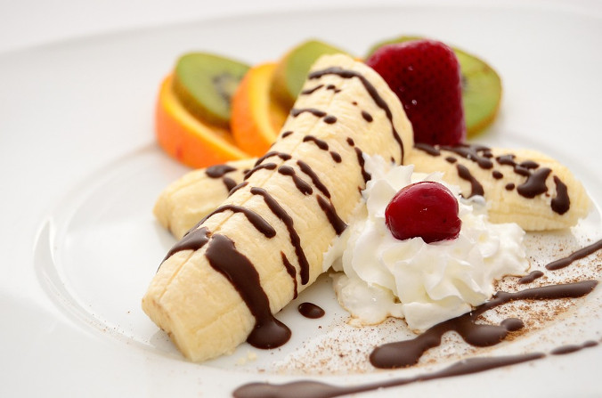 Orange and kiwi slices, a strawberry, and a sliced banana drizzled with chocolate on a white plate