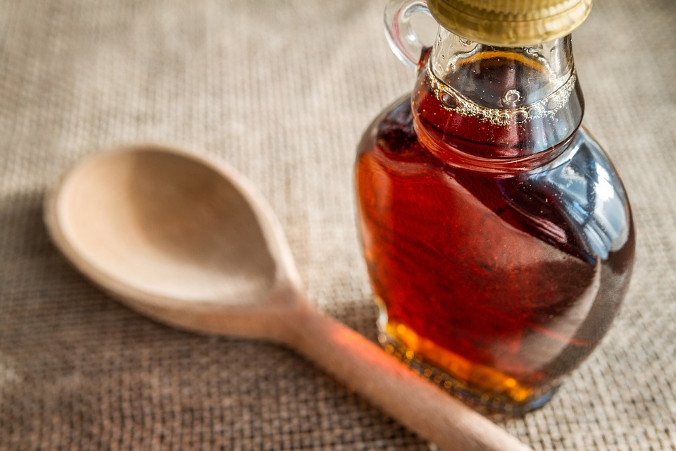 Small bottle of maple syrup next to a wooden spoon