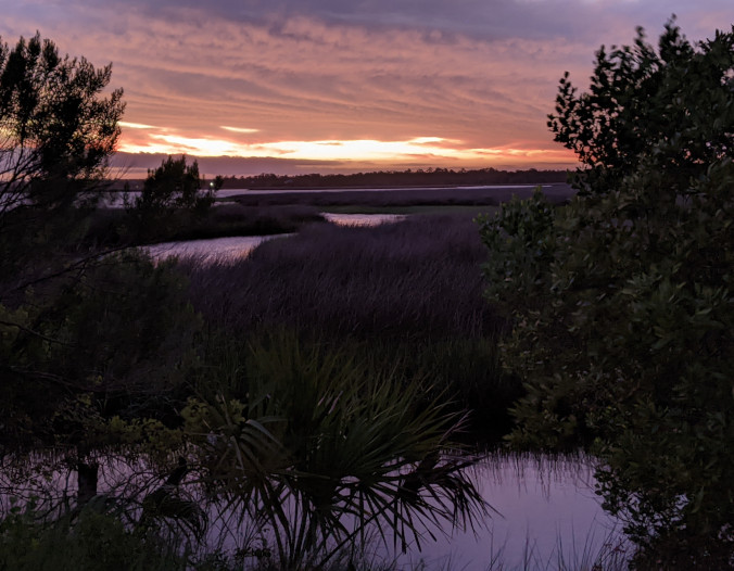 Photo picturing a purple sunset over water and marsh